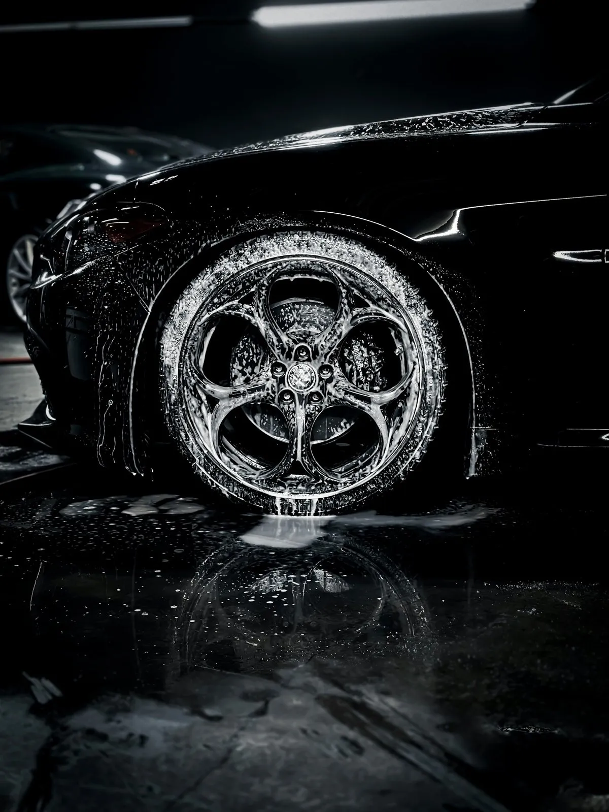 Close-up of a wet car wheel and tyre with an intricate alloy rim, dramatically lit